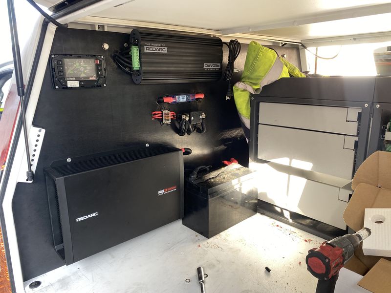 A REDARC inverter, a battery monitor and a fuse block mounted on the black lining of a work ute canopy, beside the drawer unit.
