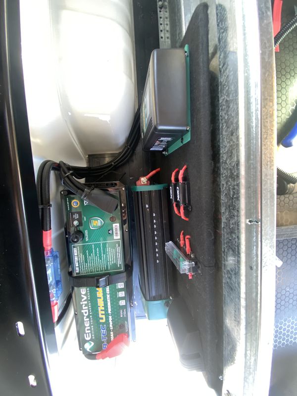 An Enerdrive lithium battery, an inverter and a row of fuse holders bolted to a board inside a vehicle canopy.