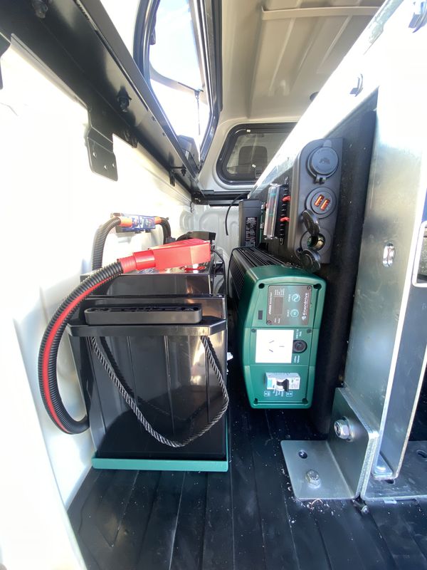 A battery, an Enerdrive charger and a twelve volt outlet panel fitted into the side wall of a ute canopy.