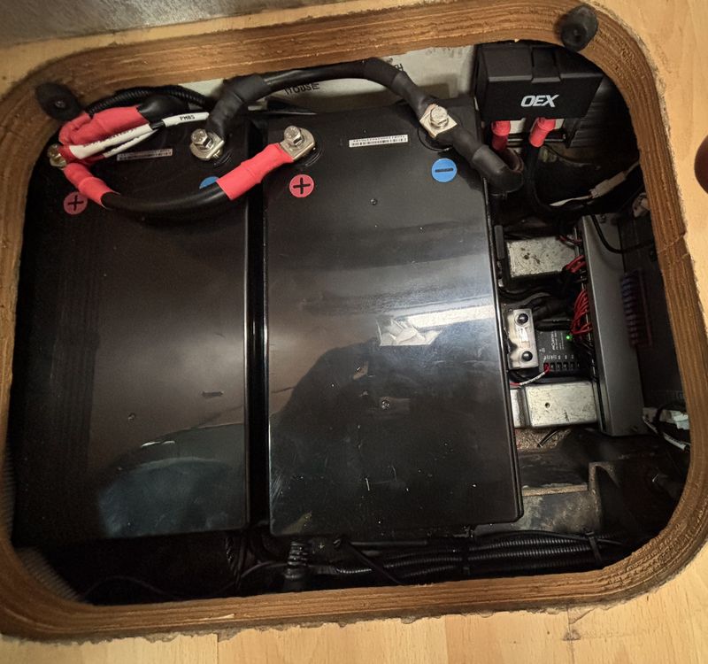 Two batteries and their fusing under a lifted floor hatch in a caravan, with heavy cable and an OEX fuse holder.